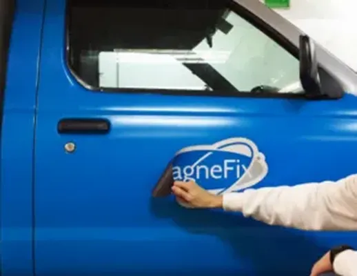 Hombre pegando un imán impreso con el logo de Magnefix en la puerta de una camioneta azul con vinil magnético donde comprar.