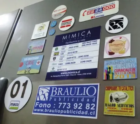 Vista desde abajo de la puerta de un refrigerador repleta de imanes de empresas, restaurantes y servicios creados con vinil magnético donde comprar.